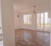 Living comedor visto desde la entrada. Piso vinílico, muros blancos, lámpara central y estufa empotrada a gas.