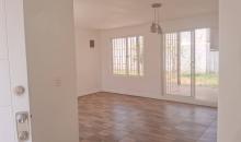 Living comedor visto desde la entrada. Piso vinílico, muros blancos, lámpara central y estufa empotrada a gas.