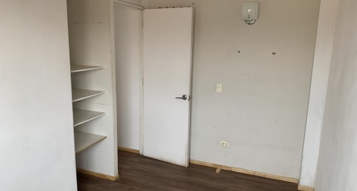 Dormitorio en segundo piso con piso flotante en tono madera, muros claros que aportan luminosidad y un closet abierto con estanterías que optimiza el almacenamiento.