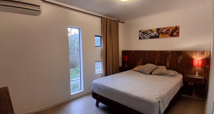 Dormitorio con cama de dos plazas, respaldo rústico de madera, dos veladores con lámparas