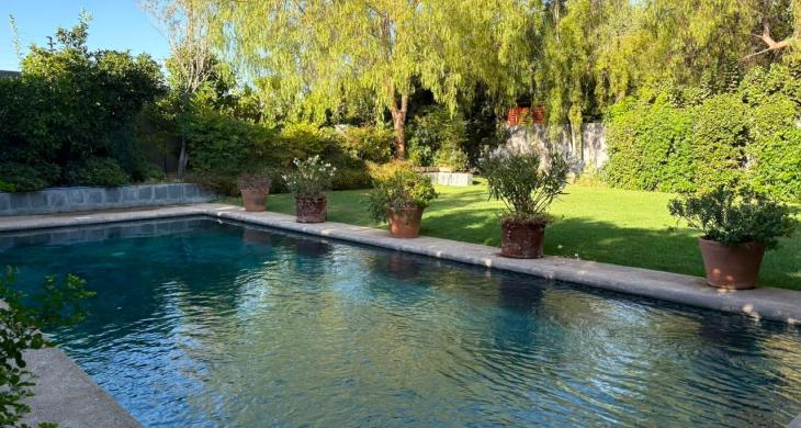 Piscina de 10x4m rodeada de un amplio jardín y árboles consolidados.